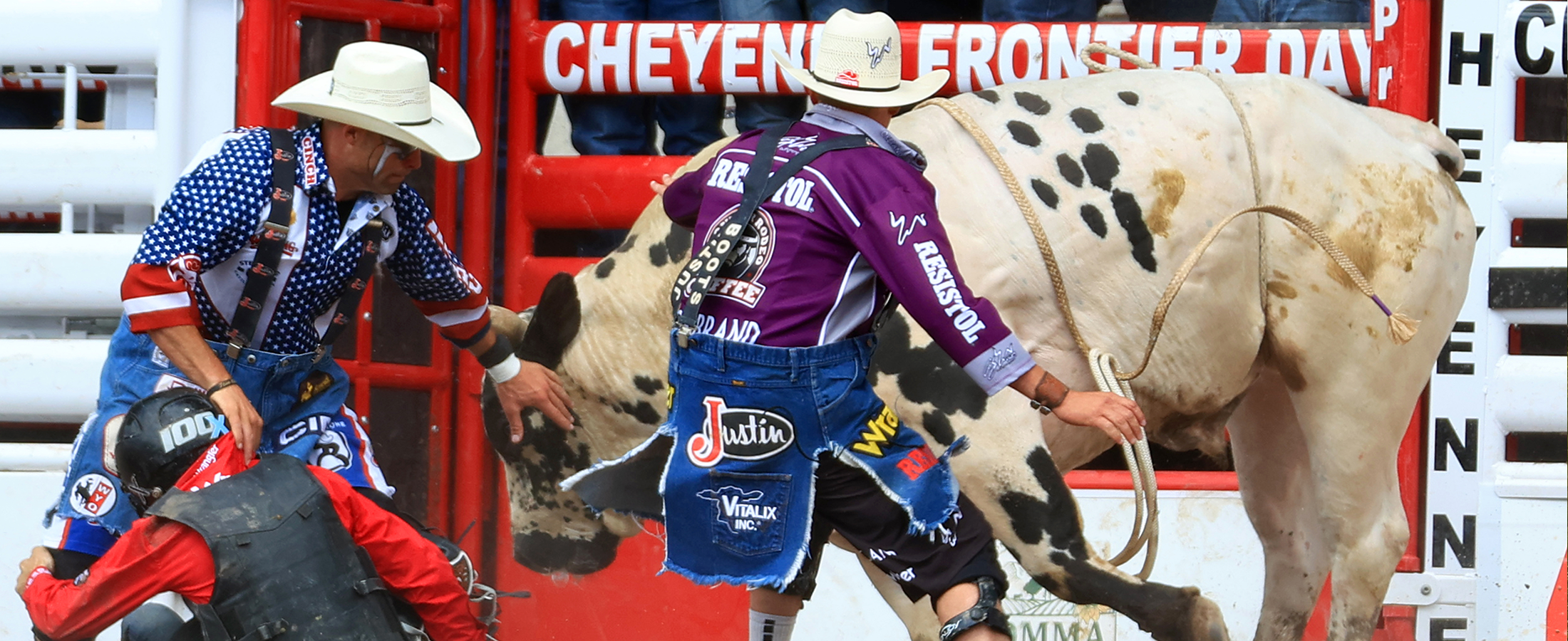 Dos payasos de rodeo y un jinete apartándose del camino de un toro.